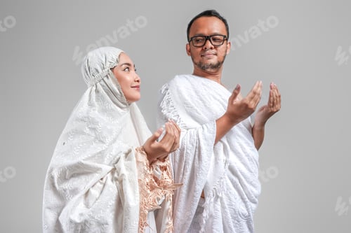 Preview: Peaceful Young Asian Muslim couple wearing ihram and prayer gown praying pose with hands.