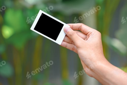 Preview: Close up of person's hand holding polaroid photo frame for mockup, outdoor nature background.