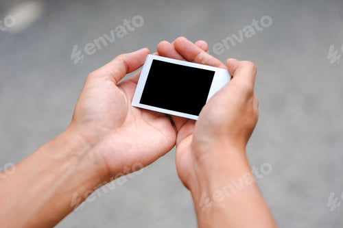 Preview: Close up of person's hand holding polaroid photo frame for mockup, outdoor nature background.