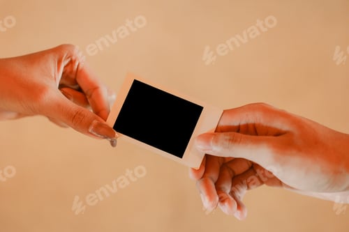 Preview: Close up of couple hands holding polaroid photo frame for mockup against isolated wall background.