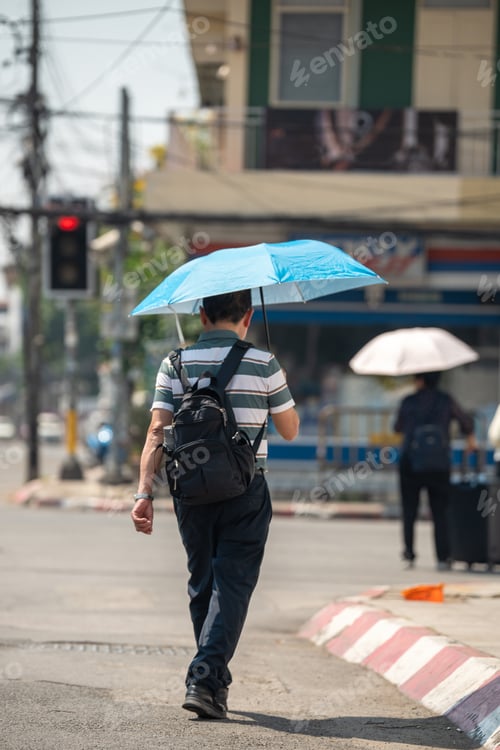 Preview: Man walking through city holding umbrella, health safety and protection from heatstroke in heatwave.