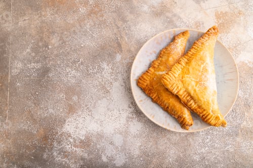Preview: Triangles Pie, Puff Pastry, Samsa with cherry jam on brown concrete, top view, flat lay, copy space
