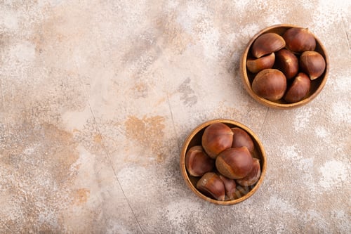 Preview: wooden bowl with raw edible Сhestnuts on brown concrete, top view, flat lay, copy space, minimalism