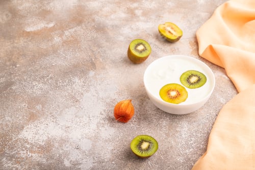 Preview: Yogurt with kiwi in white bowl on brown concrete, side view, copy space