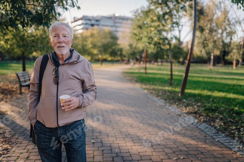 Preview: Senior man walking park path enjoying coffee