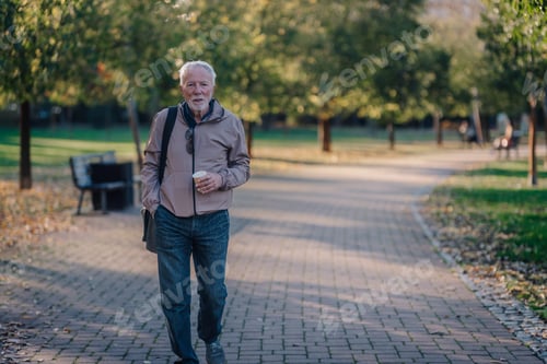 Preview: Senior man walking in park drinking coffee during autumn