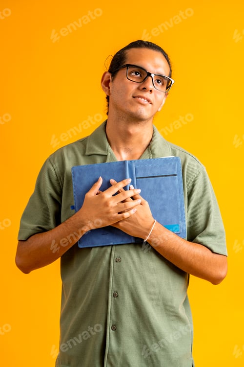Preview: Young student with glasses holding blue notebook looking up