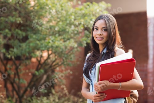 Preview: Asian female early twenties standing right at campus holding red binder white notebook, copy space