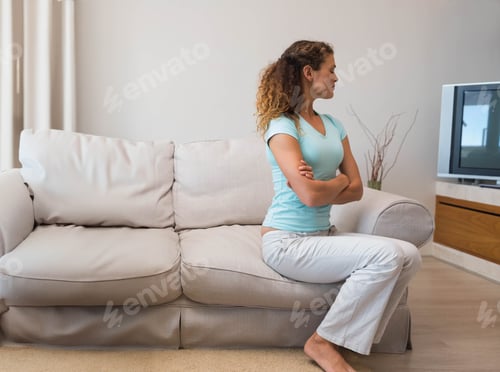 Preview: Woman sitting arms crossed facing right on beige sofa at living room with TV, copy space
