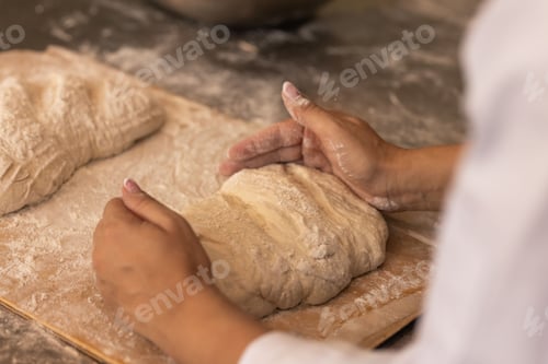 Preview: African American female baker shaping loaf dough on floured wooden board over metal counter