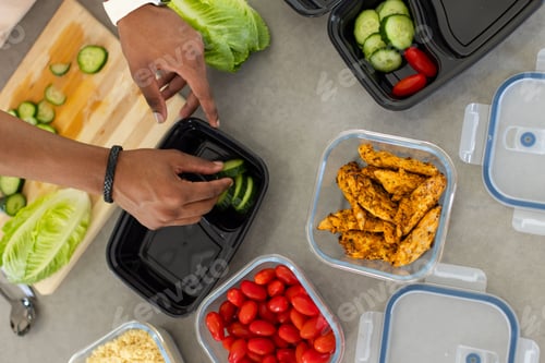 Preview: Adult male wearing white cuff placing cucumber slices into black container on counter with chicken