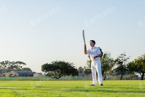 Preview: Male cricketer in whites standing on pitch holding bat, sporting wristband, looking up, copy space