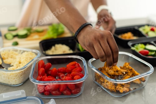 Preview: African American man placing seasoned grilled chicken into glass containers on kitchen counter