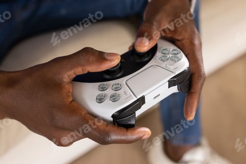 Preview: African American adult male holding white wireless controller with touchpad and buttons on sofa