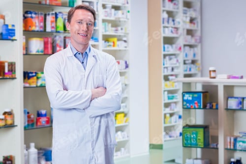 Preview: Man standing in pharmacy wearing white lab coat, holding prescription bottle by shelves and counter
