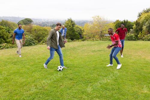 Preview: Diverse male friends playing soccer on lawn, dribbling black-and-white ball, wearing green jacket