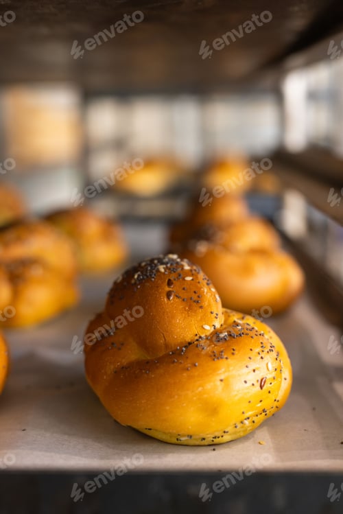 Preview: Golden knot roll resting on parchment-lined metal tray on bakery rack, gleaming with poppy seeds
