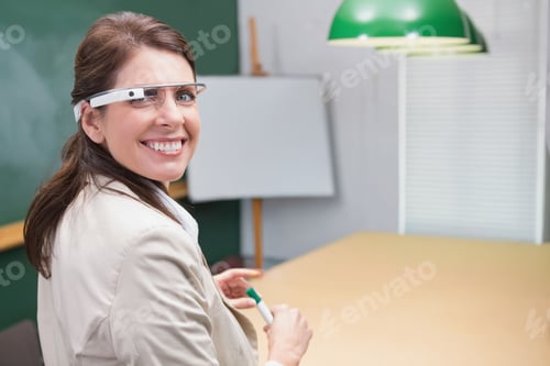 Preview: Mature female sitting at table in classroom wearing blazer and smart glasses holding green marker