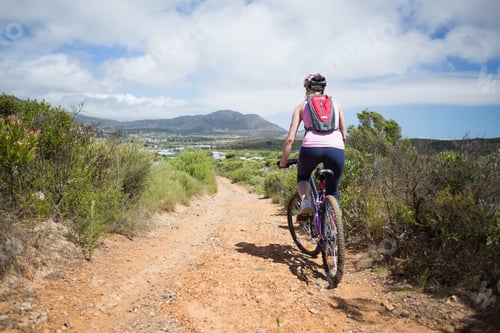 Preview: Female in twenties riding mountain bike on rocky trail with helmet and red pack, copy space