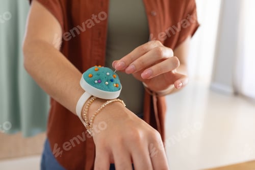 Preview: Woman using pins with teal wrist pincushion, wearing layered bracelets olive top rust shirt at home