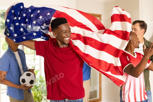 Preview: Diverse male fans wearing red tee, jersey cheering, draping US flag, holding soccer ball at home