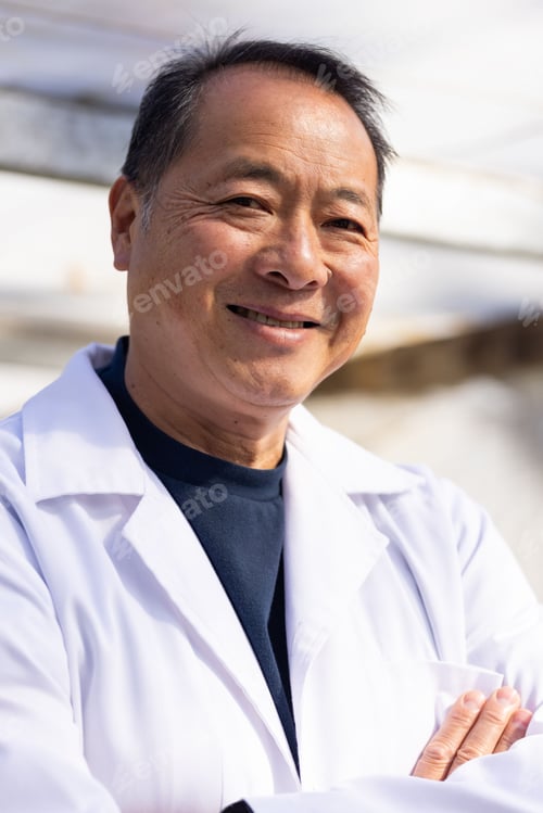Preview: Senior Chinese man standing arms crossed, smiling, wearing white lab coat and dark crewneck in lab