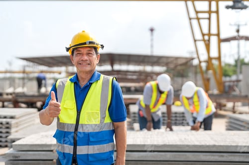 Preview: Senior Asian civil engineer showing thumbs up with team at precast concrete factory