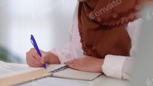 Preview: Muslim businesswoman writing notes planning work strategy at modern office desk wearing traditional