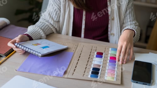 Preview: Fashion designer selecting color palette from fabric swatches at studio workspace with notebook sket