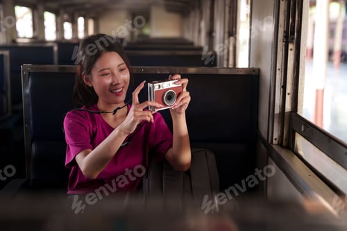 Preview: Asian woman tourist taking photos with vintage camera on train journey