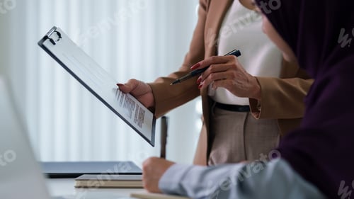 Preview: Businesswoman Reviewing Contract Document With Colleague Signing Agreement Partnership Collaboration