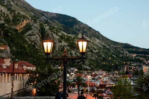 Preview: Glowing street lamps overlooking Kotor bay marina and mountains at evening in Montenegro