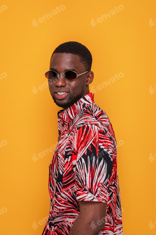 Preview: African American man in red tropical shirt and sunglasses looking at camera on yellow background