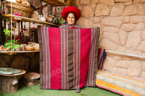Preview: Indigenous Andean woman holding traditional woven textile in a rural weaving workshop