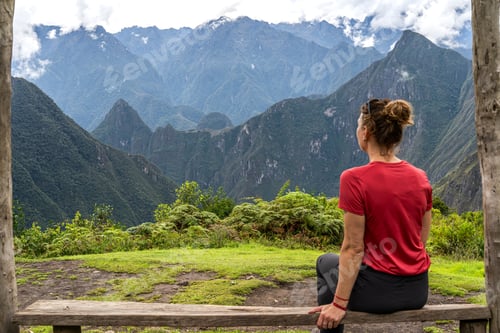 Preview: Female traveler sitting on wooden bench overlooking dramatic Andes mountains in Peru