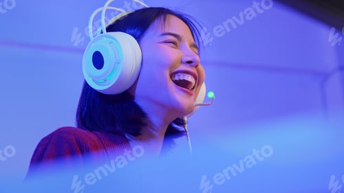 Preview: Excited young Asian girl playing video game with gaming headset and controller at home, esports onli