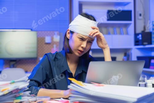 Preview: Injured young Asian office worker wearing head bandage while working on laptop in office, health and