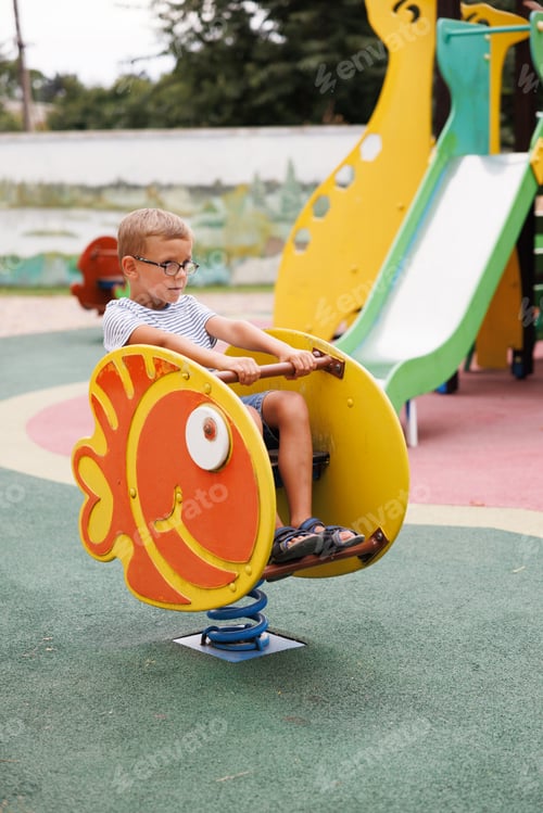 Preview: Young boy playing on fish-shaped spring rocker at playground