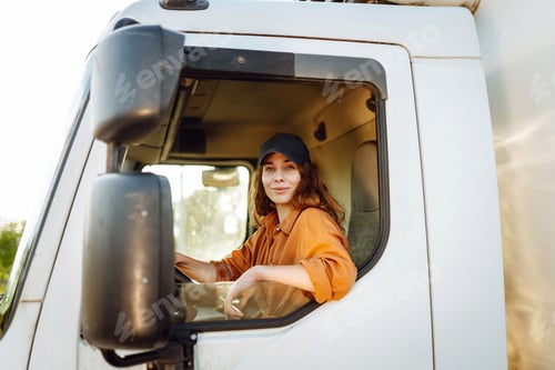 Preview: Portrait of beautiful young woman professional truck driver driving a big truck. Inside of vehicle