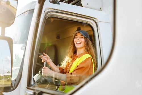 Preview: Portrait of beautiful young woman professional truck driver driving a big truck. Inside of vehicle
