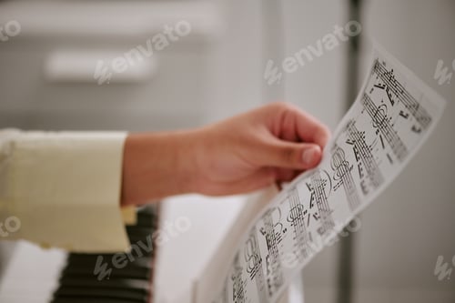 Preview: Close up of teenager hand holding sheet music near piano, reviewing notes during practice and music