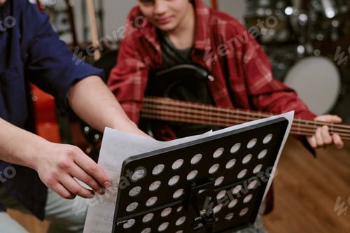 Preview: Teenager musician practicing bass guitar with instructor, reading sheet music during lesson in studi