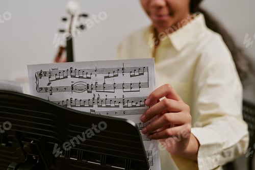 Preview: Teenager girl arranging sheet music on stand during string instrument practice, focusing on music ed