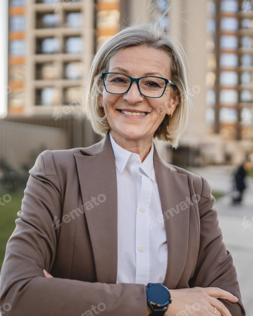Preview: One mature business woman stands with folded arms outdoors in front of a building