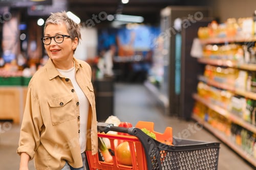 Preview: Smiling mature woman pushing shopping cart in supermarket