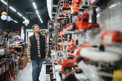 Preview: Portrait of young bearded man buying modern electric drill while standing in tool. Hardware construc