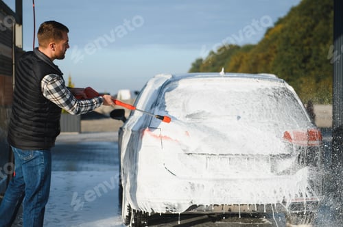 Preview: A man washes off the foam while washing the car. A vehicle is engulfed in soapy foam during a car wa