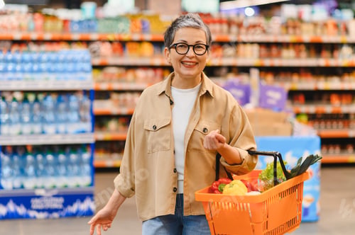 Preview: Mature woman smiling while grocery shopping in supermarket
