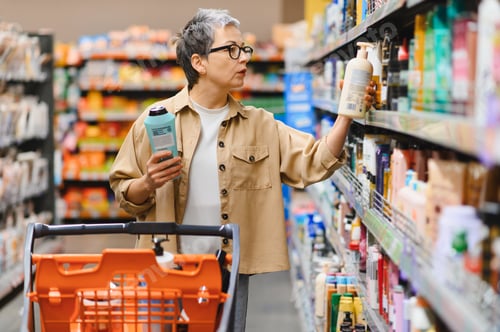 Preview: Woman comparing body care products in supermarket aisle