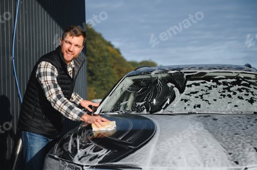 Preview: A man washes a car with a sponge at a self-service car wash